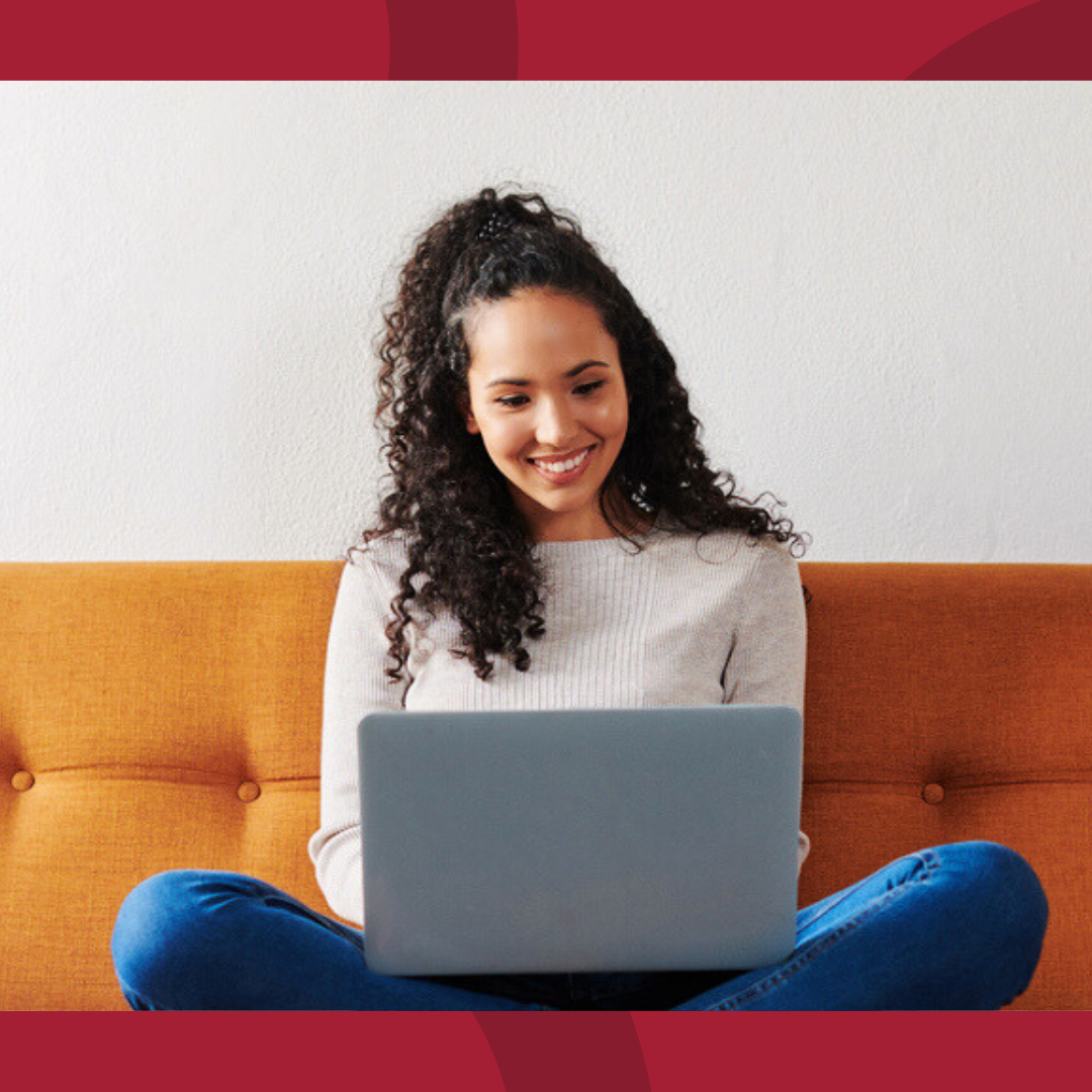 A woman is sitting on her couch and looking at her laptop.